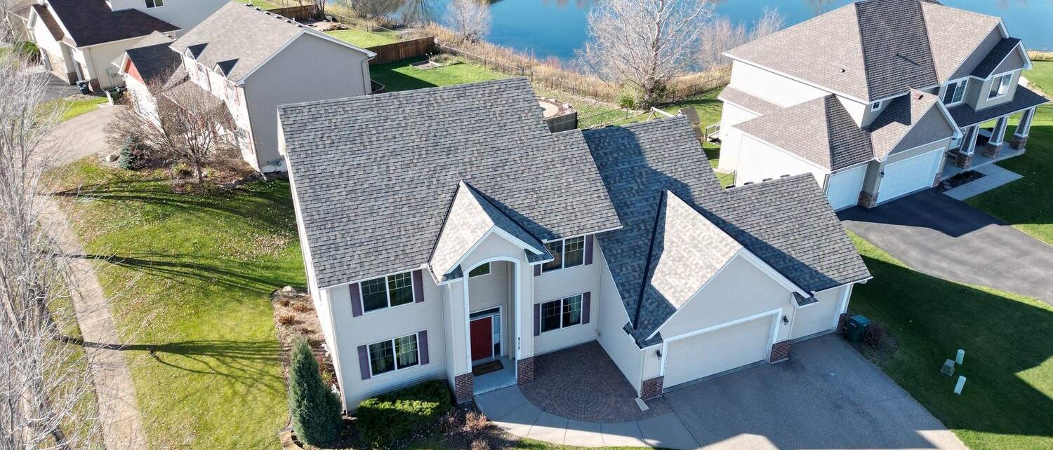 Aerial view of a replaced asphalt shingle roof on a two-story home by a pond