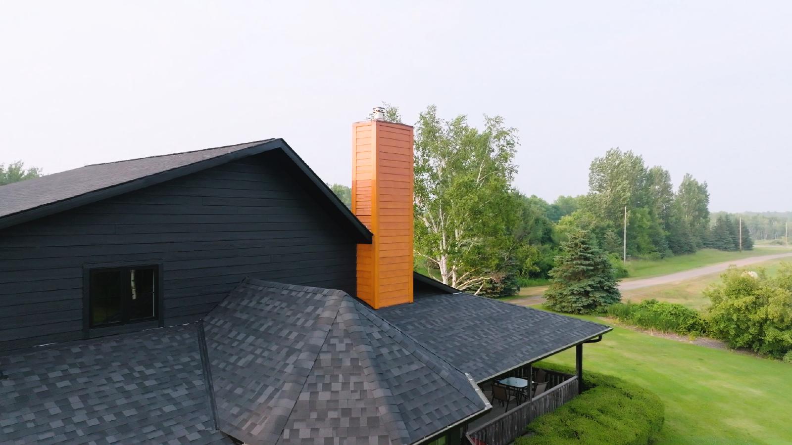 A contractor installing asphalt shingles on a residential roof with fiber cement siding. | Omega Exteriors