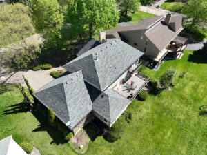 A professional installing asphalt shingles on a residential roof with new siding and gutters. | Omega Exteriors